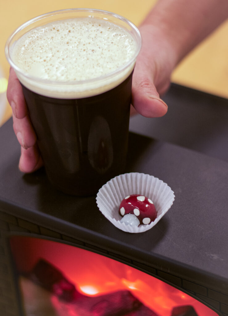 Cup of nitro cold brew coffee and a red and white mushroom-shaped bonbon on top of a fireplace lamp.